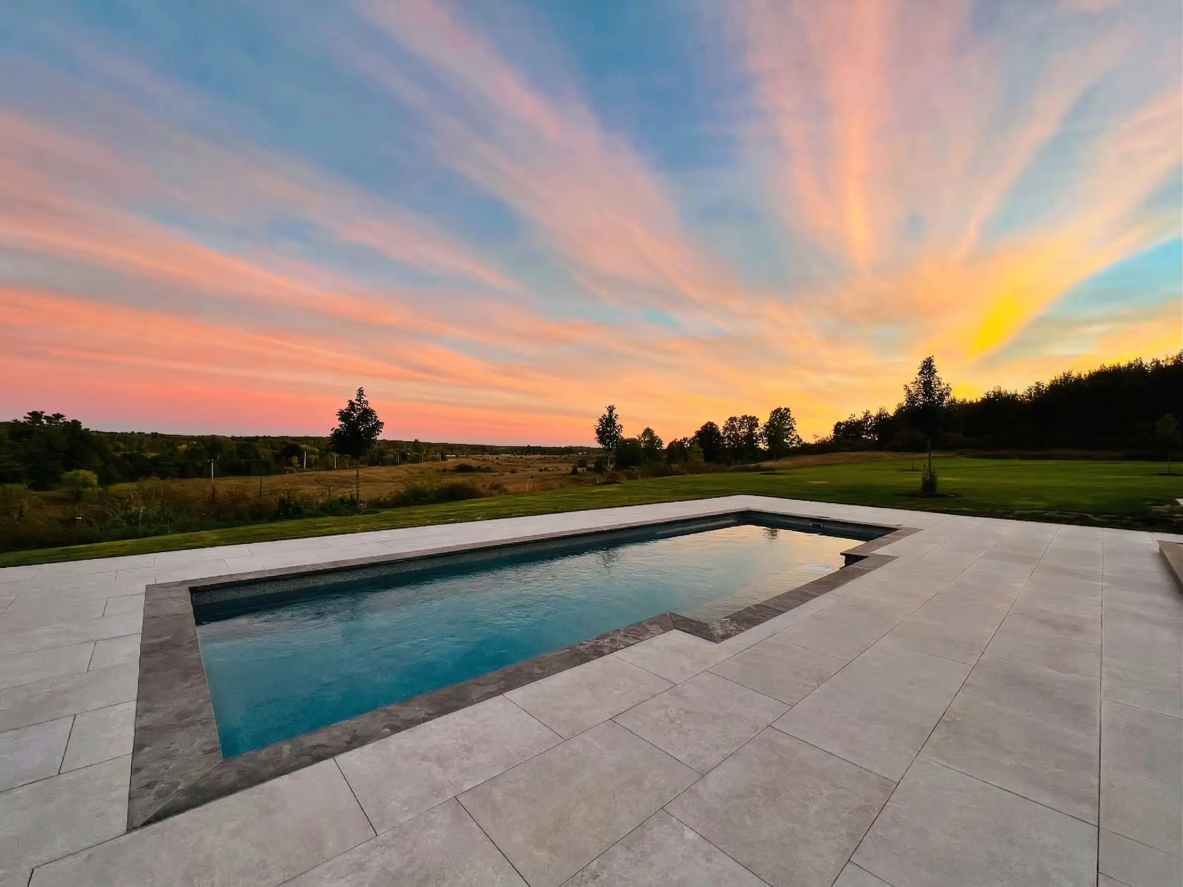 Modern rectangular inground pool reflecting sunset sky